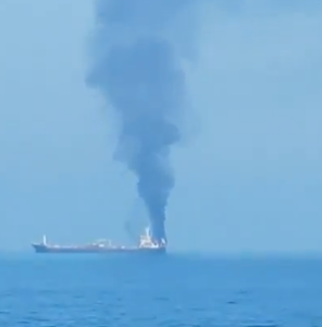 Vessels anchored near the Strait of Hormuz off Oman coast with warships in background.