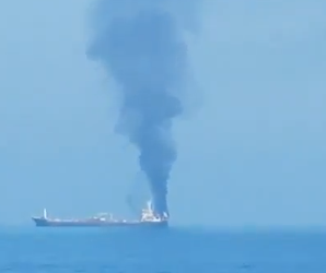 Vessels anchored near the Strait of Hormuz off Oman coast with warships in background.