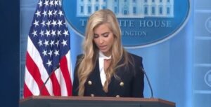 Katie Zacharia speaks to reporters at the podium in the White House press briefing room.